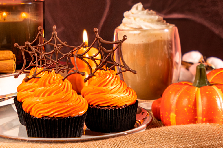 Cupcakes with orange frosting on a table with Halloween decorations