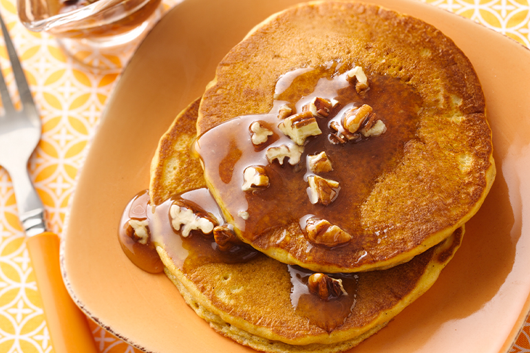 Pancakes on an orange plate with syrup on top