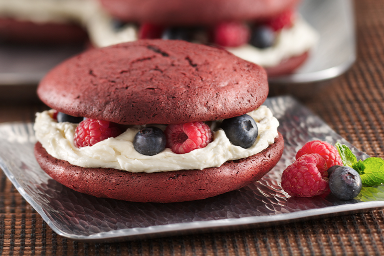 Red velvet whoopie pies filled with white cream and berries