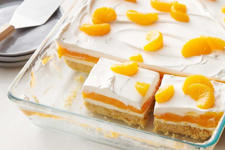 Clear pan with white spatula and three grey plates, mandarin oranges on top of white whipped cream
