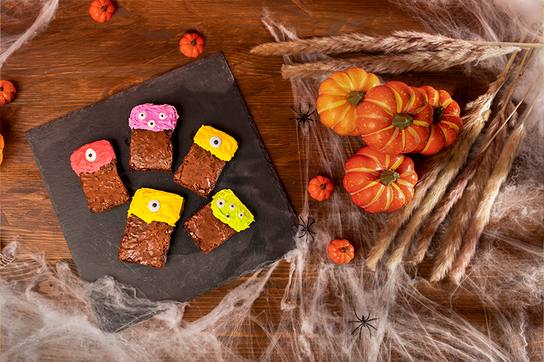 Brownies decorados con betún de colores sobre mesa con decoración de Halloween