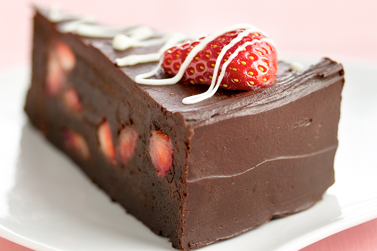 Pastel de chocolate con fresas en el interior decorado con chocolate blanco y una fresa