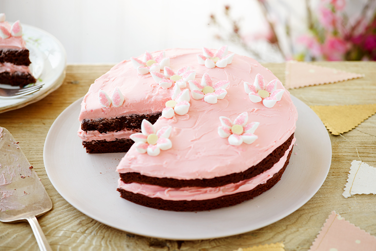 Pastel de brownie de dos capas con frosting rosa en medio y encima decorado con flores de malvavisco