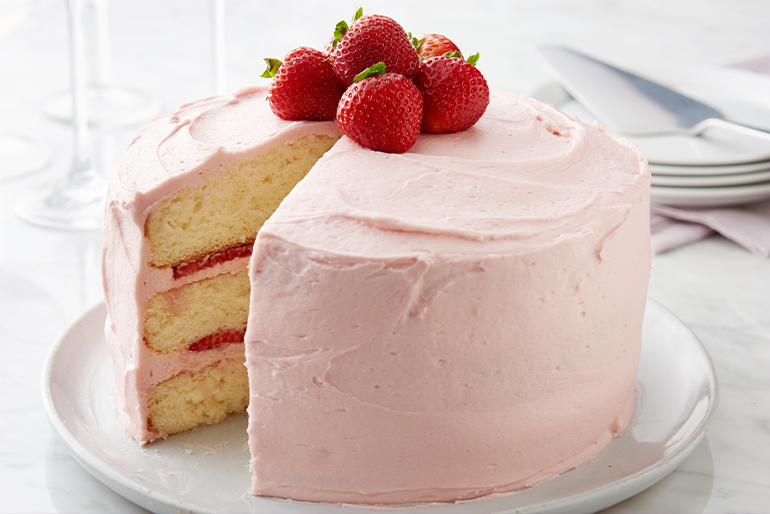 Pastel de vainilla cubierto con frosting de fresa con fresas frescas en la parte superior